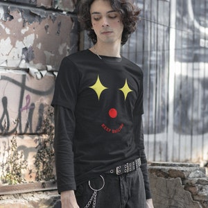 Puede incluir: Una camiseta negra de manga larga con un gr&aacute;fico de cara sonriente amarilla y el texto "Keep Smiling" en rojo.