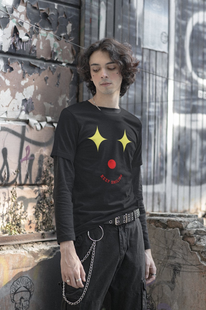 Puede incluir: Una camiseta negra de manga larga con un gr&aacute;fico de cara sonriente amarilla y el texto "Keep Smiling" en rojo.