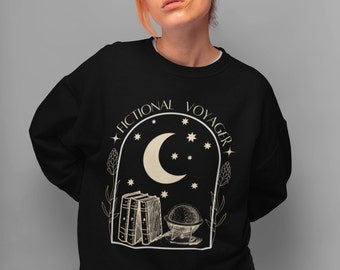 Op de afbeelding: Zwart sweatshirt met een wit grafisch ontwerp met een halve maan, sterren, boeken en een globe. De tekst "Fictional Voyager" staat in een cirkel rond het ontwerp.