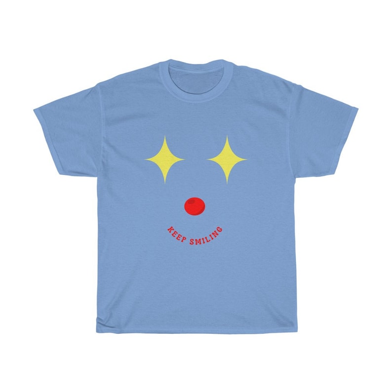 Puede incluir: Camiseta azul claro con un dise&ntilde;o de estrellas amarillas y una nariz roja, con el texto "KEEP SMILING" debajo.