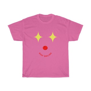 Puede incluir: Camiseta rosa con un gr&aacute;fico de cara sonriente. La cara tiene estrellas amarillas para los ojos y una nariz roja. El texto "KEEP SMILING" est&aacute; escrito en un arco rojo debajo de la cara.