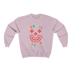May include: A pink sweatshirt with the text "DOWN TO CLOWN" in rainbow colors. A stylized clown face with a red nose and blue eyes is in the center of the text.