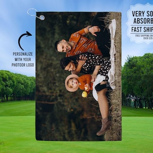 May include: A personalized golf towel featuring a family of three sitting on a blanket in a forest setting. The towel is white with a green border and has the text "PERSONALIZE WITH YOUR PHOTOOR LOGO" on the left side.
