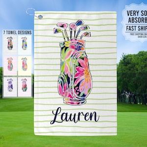 May include: A white golf towel with green stripes and a floral print golf bag design. The towel has the name "Lauren" printed on it.  7 TOWEL DESIGNS is printed on the left side of the towel.