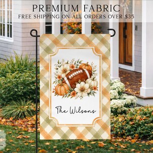 May include: A rectangular garden flag featuring a tan and olive green plaid border. The center displays a white background with a decorative frame containing a brown football, orange pumpkins, and white flowers. The text The Wilsons is printed below.