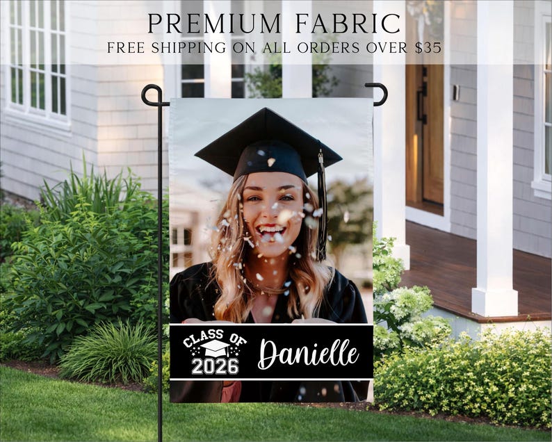 K&ouml;nnte beinhalten: Eine Gartenflagge zur Feier des Abschlusses mit einem Foto einer l&auml;chelnden Absolventin in Hut und Robe. Die Flagge enth&auml;lt den Text "Class of 2026" und den Namen "Danielle" auf einem schwarzen Banner. Oben auf der Flagge steht "Premium Fabric".