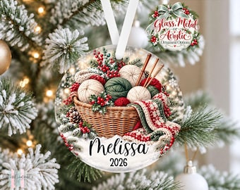 May include: A round Christmas ornament featuring a woven basket filled with yarn balls, knitting needles, pine branches, and red berries. A patterned scarf drapes over the side. The text Melissa and 2026 is printed in black on the lower portion.