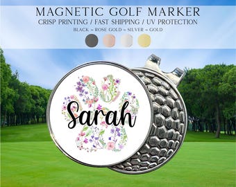 Op de afbeelding: Een ronde magnetische golfmarker met een wit middenstuk, een kleurrijk bloemig pootafdrukontwerp en de naam Sarah in zwarte schrijfletters. De marker heeft een metallic zilveren, getextureerde rand met een honingraatpatroon en een metalen clip.