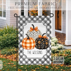 May include: A rectangular garden flag featuring a black and white buffalo check background. The center displays three pumpkins: one orange plaid, one white with black vines, and one black with yellow sunflowers. The text THE WILSONS is printed below.