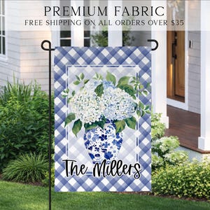 May include: A blue and white gingham garden flag featuring a floral design. The flag displays a blue and white vase filled with white and blue hydrangeas. The text "The Millers" is printed on the bottom.