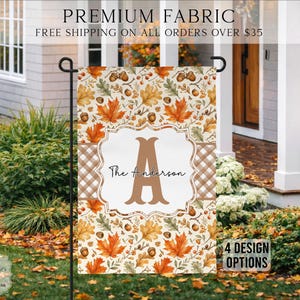 May include: A rectangular garden flag featuring an autumn-themed pattern of orange, yellow, and brown maple leaves and acorns. A central white rectangular plaque displays a large brown letter A and the text The Anderson in black script.