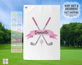 May include: White golf towel with a pink watercolor banner that says "Danielle" and two crossed golf clubs with a golf ball on a tee. The towel is for golf enthusiasts.