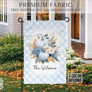 May include: A rectangular garden flag featuring a light blue and white buffalo check pattern. The center displays a white panel with a floral arrangement of two light blue pumpkins, blue roses, and orange flowers, with the text The Wilsons below.