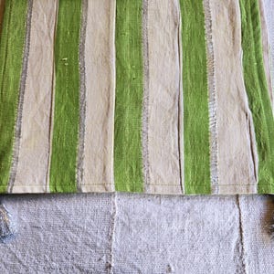 Könnte beinhalten: Ein grün-beige gestreifter Tischläufer mit silbernen Quasten an jedem Ende. Der Läufer hat vertikale Streifen in Hellgrün und Beige. Die Quasten sind silbergrau. Der Stoff scheint strukturiert zu sein.