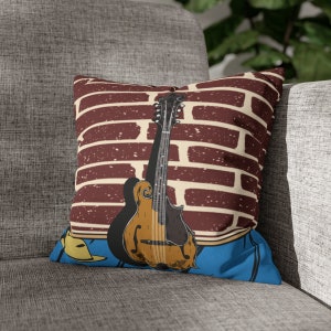 May include: A decorative throw pillow with a brick wall background and a mandolin in the center. The mandolin is brown and has a blue and yellow design on the bottom.