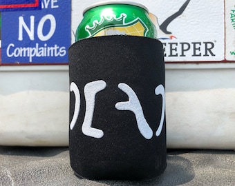 May include: A black foam beverage insulator sleeve featuring a white graphic design on the front. The sleeve is wrapped around a green aluminum can with a crown logo. The design consists of stylized white shapes resembling abstract symbols.