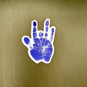 May include: A blue handprint sticker with a white outline. The hand is making the 'rock on' hand gesture.