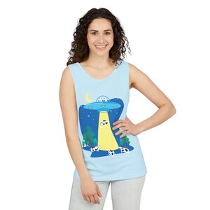Puede incluir: Camiseta sin mangas azul claro con un diseño humorístico de un OVNI abduciendo vacas. El diseño incluye un cielo nocturno con estrellas, una luna creciente y árboles verdes. La camiseta sin mangas es sin mangas y tiene cuello redondo.