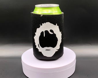 May include: A black foam beverage insulator sleeve featuring a white graphic silhouette of a person with curly hair and a beard. The sleeve is wrapped around a light green aluminum beverage can with visible text reading sugar and calories.