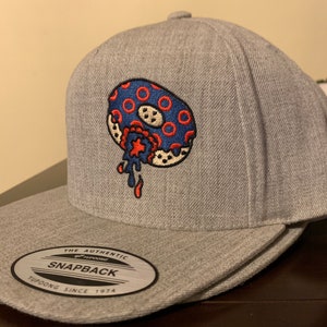 May include: Gray baseball cap with a red, white, and blue donut graphic. The donut has sprinkles and a red star. The text "The Authentic Snapback Yupoong Since 1974" is on the back of the cap.