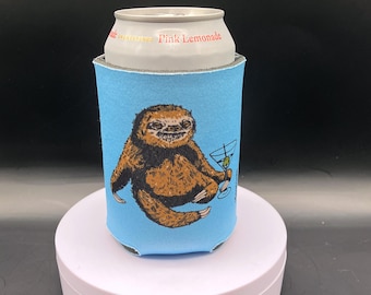 May include: A light blue can cooler featuring a brown sloth holding a martini. The sloth is smiling and the drink has a green olive. The can cooler is holding a can of Pink Lemonade.