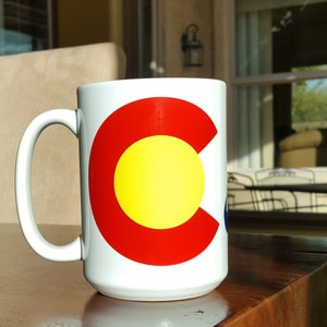 May include: White ceramic coffee mug with a red, yellow, and blue Colorado state flag design.
