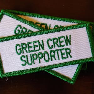 May include: Three white embroidered patches with green borders. The top patch says "Green Crew" and the bottom patch says "Supporter".