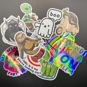 May include: A collection of colorful stickers featuring various designs, including a ghost, a sloth, a scooter, a pickle jar, and a holographic sticker that says "Sounds like a you problem".