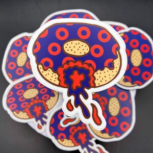 May include: A stack of blue and red donut stickers with white frosting and red and blue dripping icing. The donuts have a pattern of red rings on a blue background.