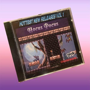 May include: A CD case featuring the game "Hocus Pocus" from the "Hottest New Releases Vol 1" series. The game's cover art depicts a pixelated scene with a full moon, bats, and a character on a platform.