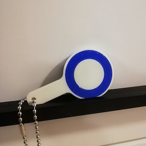 May include: White keychain with a blue circle and a white inner circle. The keychain has a silver chain.