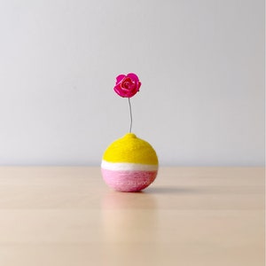 Könnte beinhalten: Eine kleine, runde, gelbe und rosafarbene Filzvase mit einer einzelnen rosa Blume.