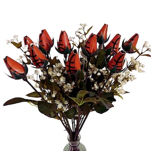May include: A bouquet of orange and black basketball-themed roses in a clear glass vase. The roses are arranged in a vase with green leaves and white flowers.