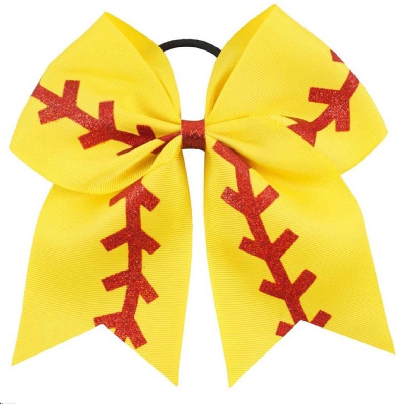 May include: A yellow cheer bow with a red glitter softball design. The bow has a black elastic band.