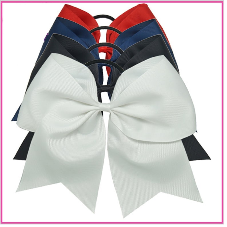 May include: A set of four cheer bows in red, navy blue, black, and white. The bows are tied together with a black elastic band.