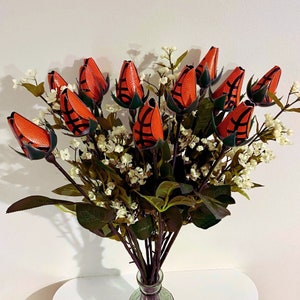 May include: A bouquet of artificial flowers with orange and black basketball-themed blooms. The flowers are arranged in a vase and have green leaves.