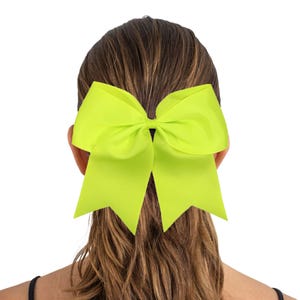 May include: A bright neon green cheer bow with a large, double-looped bow.