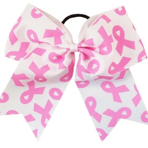 May include: A white cheer bow with a pink ribbon pattern. The bow is attached to a black elastic hair tie.