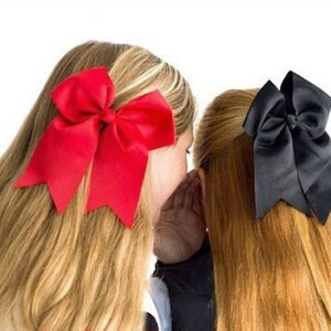 May include: Two girls with long hair, one with a red bow and the other with a black bow.