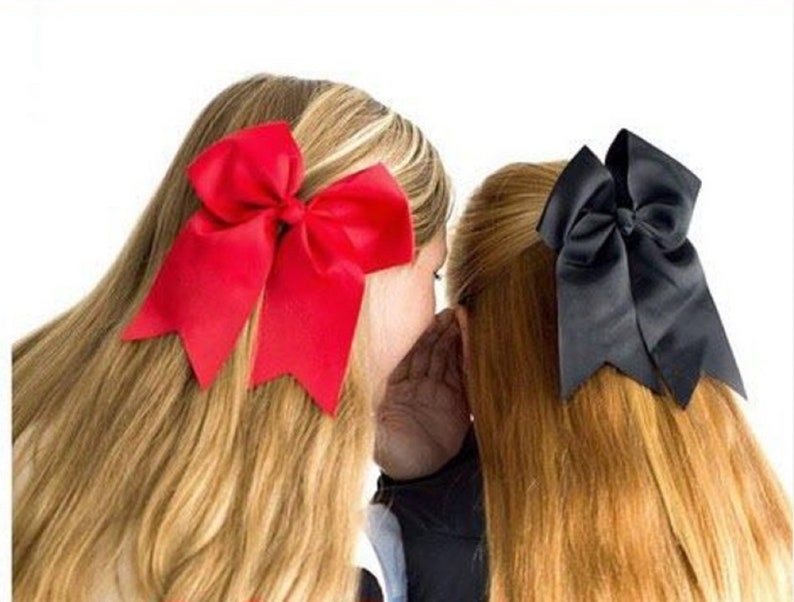May include: Two girls with long hair, one with a red bow and the other with a black bow.