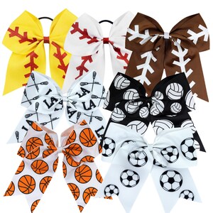 May include: Six different hair bows with various sports themes. The bows are white with black and red accents. The sports themes include baseball, basketball, football, lacrosse, softball, and volleyball.