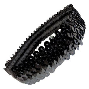 May include: A black sequin headband. The headband is made of a black elastic band covered in small, round, shiny black sequins. The sequins are densely packed together, creating a shimmering effect. The headband is designed to be worn around the head.