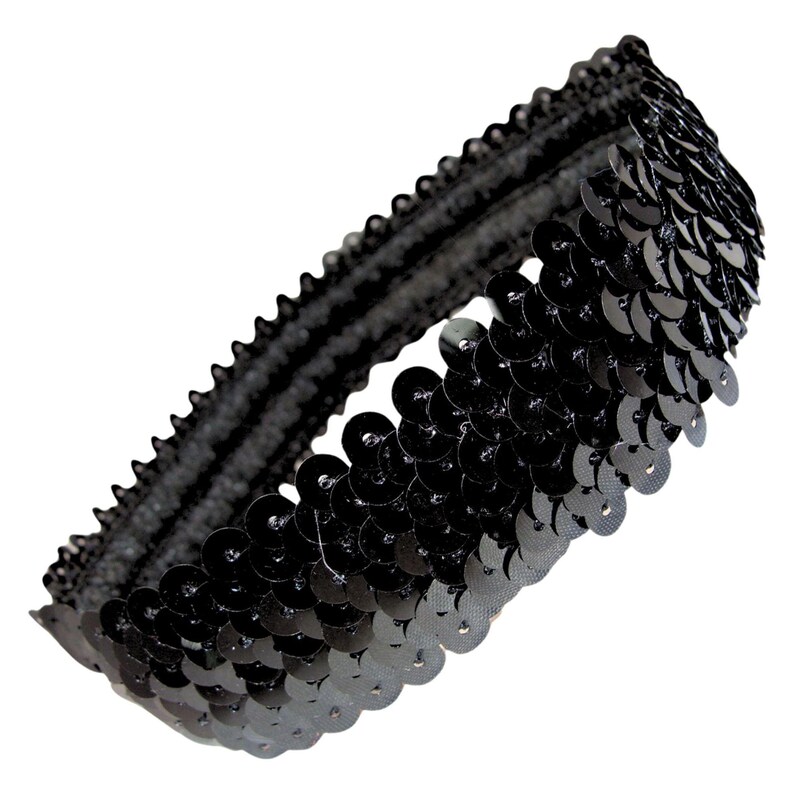 May include: A black sequin headband. The headband is made of a black elastic band covered in small, round, shiny black sequins. The sequins are densely packed together, creating a shimmering effect. The headband is designed to be worn around the head.