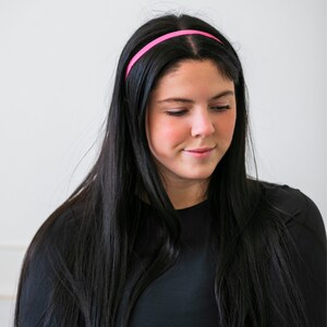 May include: A woman with long black hair wearing a pink headband and a black long-sleeved shirt.
