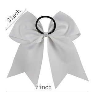 May include: White cheer bow with a 7 inch length and 3 inch width. The bow is attached to a black elastic hair tie.