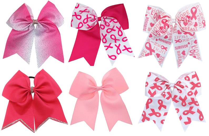 May include: Six pink and white cheer bows with different designs. The bows feature pink ribbons with white text and pink ribbons with white and pink ribbon designs. The bows are tied with a white ribbon.