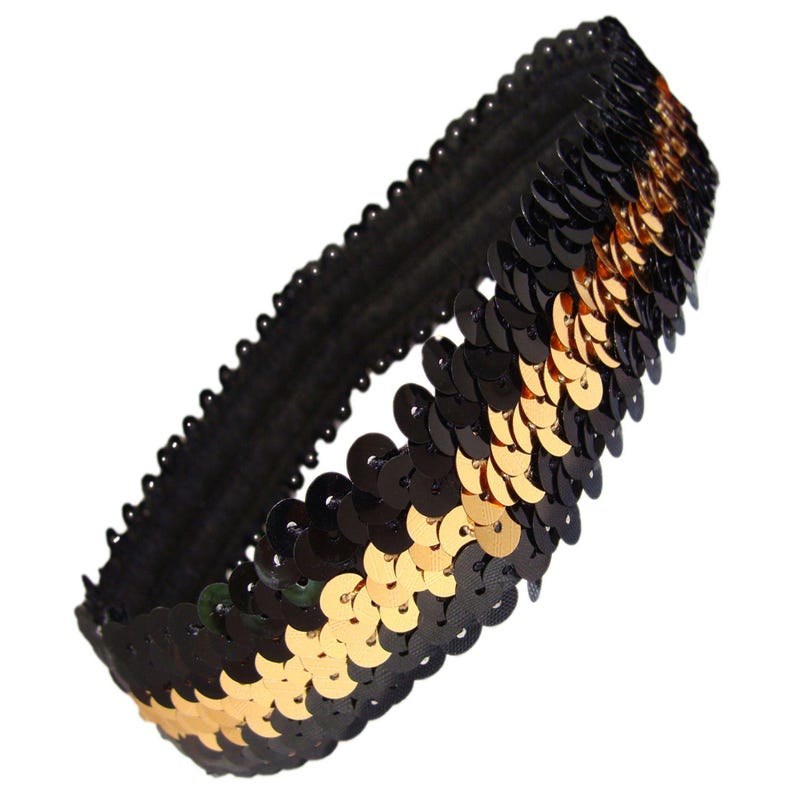 May include: A black and gold sequin headband. The headband is made of a black elastic band covered in black and gold sequins. The sequins are arranged in rows and create a shimmering effect. The headband is designed to be worn around the head.