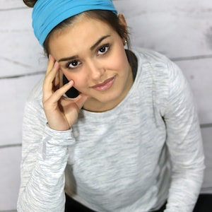 May include: A woman wearing a light blue headband and a gray long-sleeve shirt. The woman is sitting and looking up at the camera. She is wearing a black watch with a pink band.