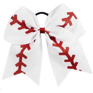 May include: White baseball-themed hair bow with red glitter stitching detail. The bow is attached to a black elastic hair tie. A fun accessory for sports fans or cheerleaders.