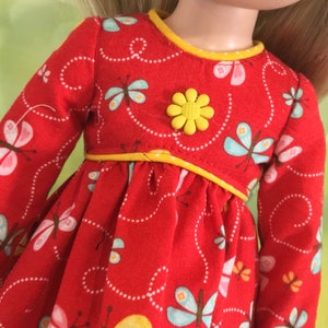 Op de afbeelding: Rode poppenjurk met een gele zoom en een gele bloemknop. De jurk heeft een vlinderprint.